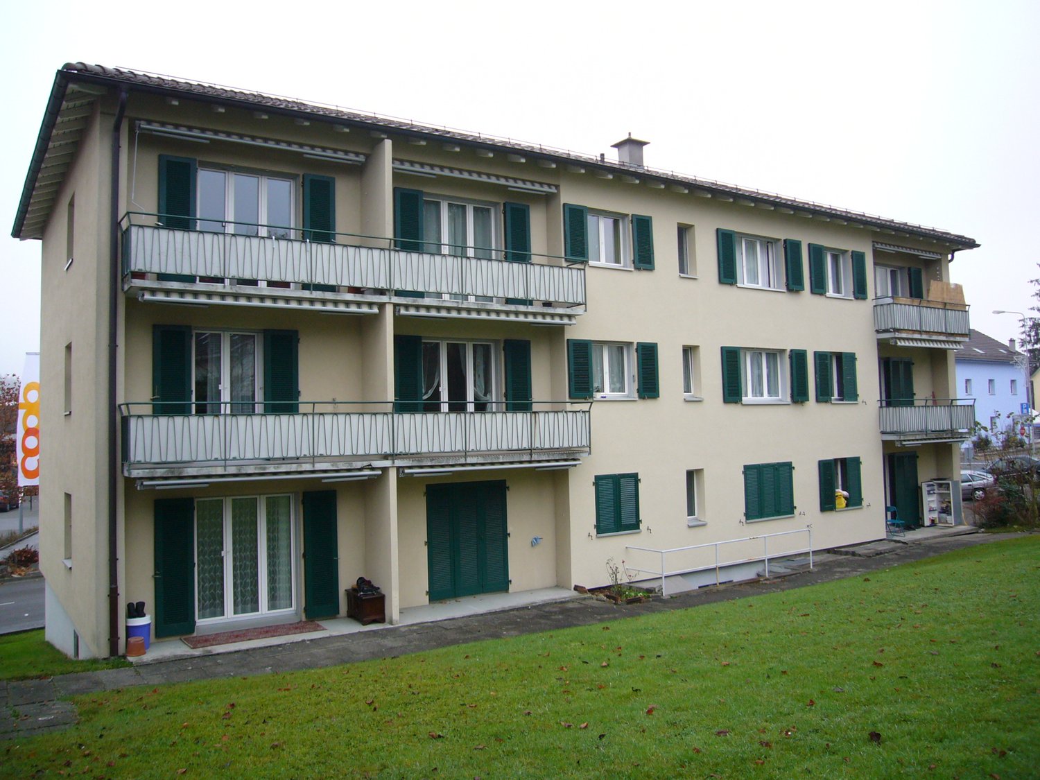 3 story apartment building, beige walls, green shutters, balcony on the top floor