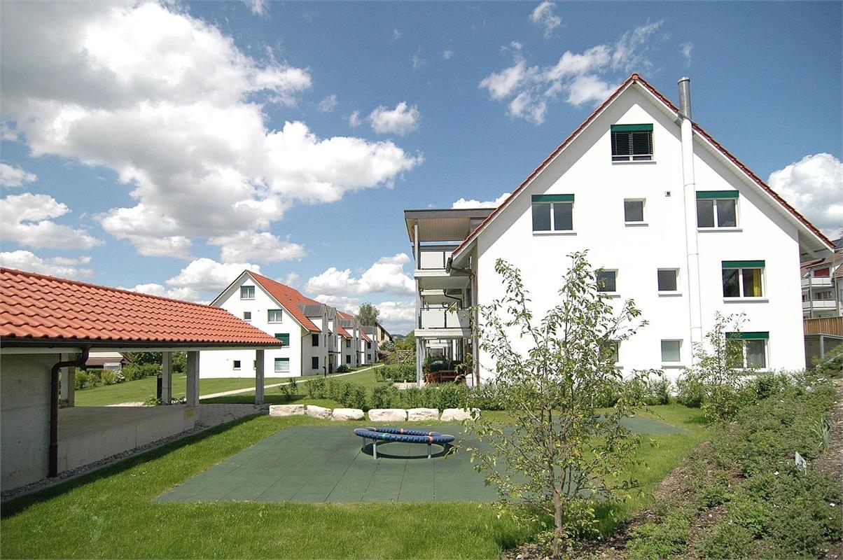 Row of white townhouses, green roofs, red roofs, garden, playground