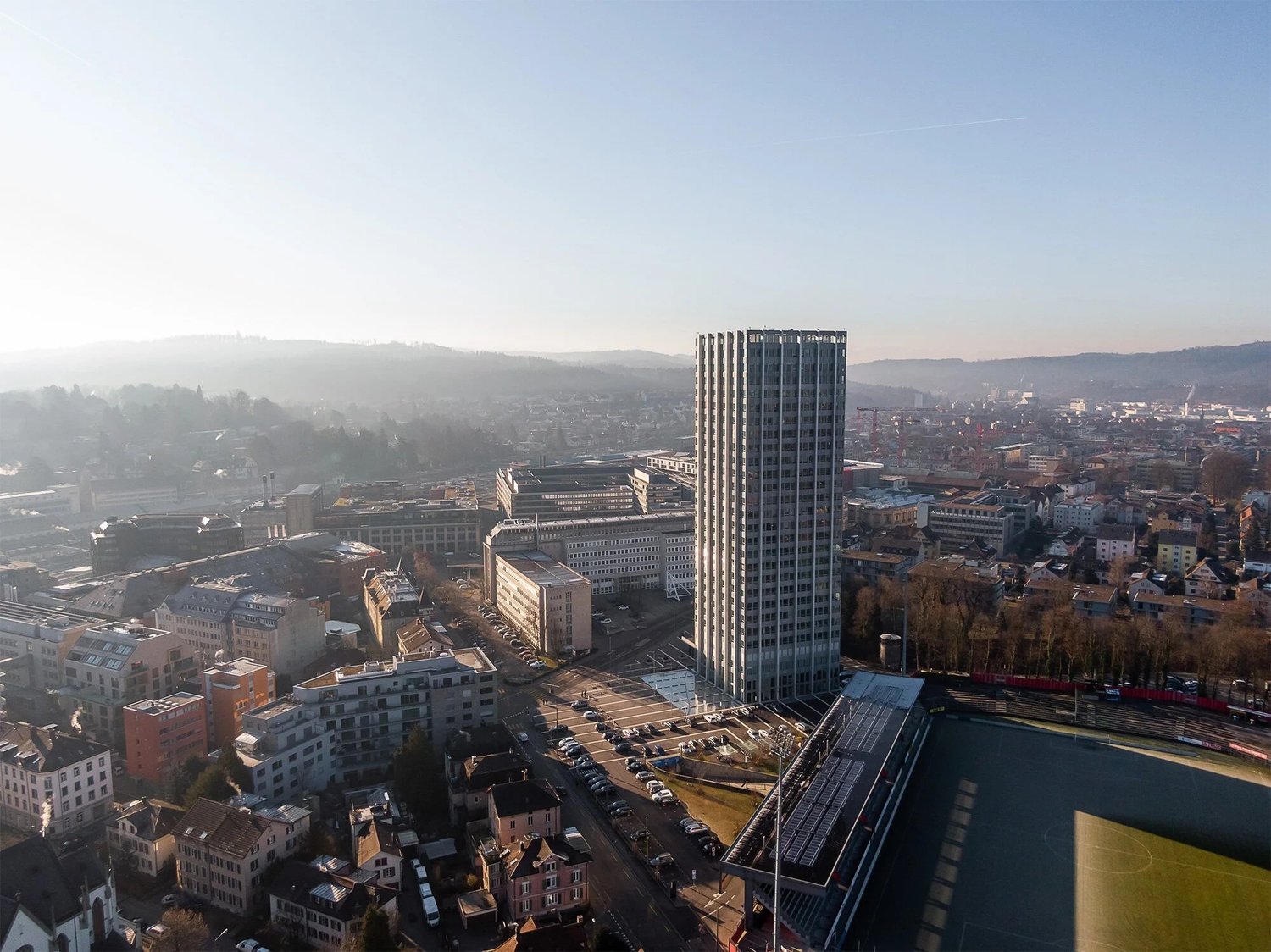 Aerial view of a city with a tall building, parking lot, and surrounding buildings