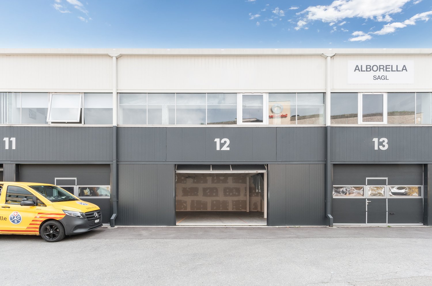 Commercial building with three garages, yellow van parked in front, large windows, gray exterior, number 11, 12, and 13 on the building