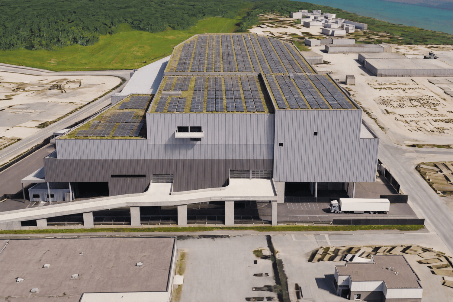 Large building with rooftop solar panels, a gray exterior, concrete walkways, a truck, and a parking area