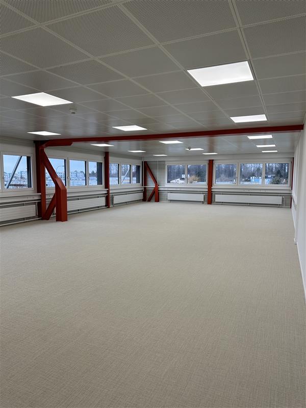 large open space, white carpet, multiple large windows, exposed steel beams