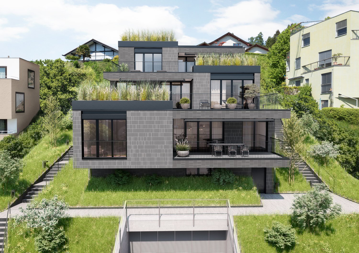 Modern two-story house with a flat roof, large windows, and a balcony on the upper level. The house has a raised ground floor with a parking area underneath. The exterior is predominantly dark-colored with a mix of materials including glass, metal, and wo