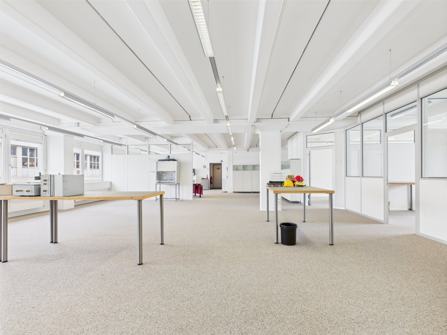 Empty office room with desks and fluorescent ceiling lights, carpeted floor