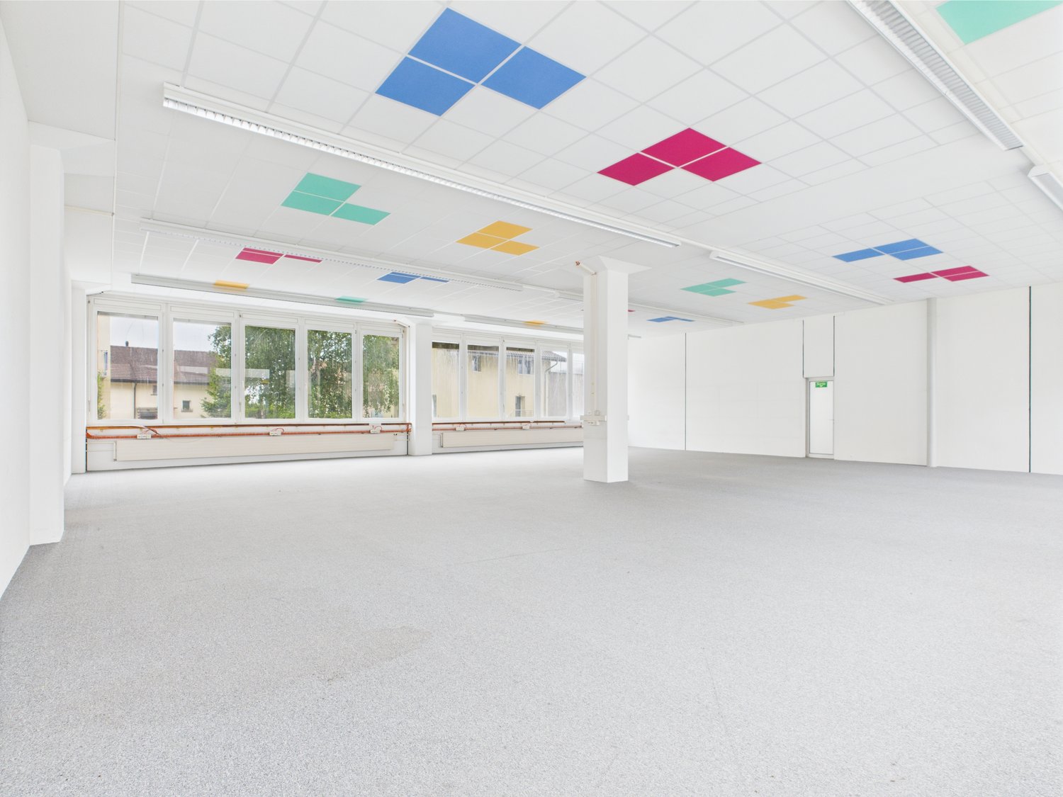spacious room, white walls, ceiling with multicolored square panels, large windows, carpeted floor