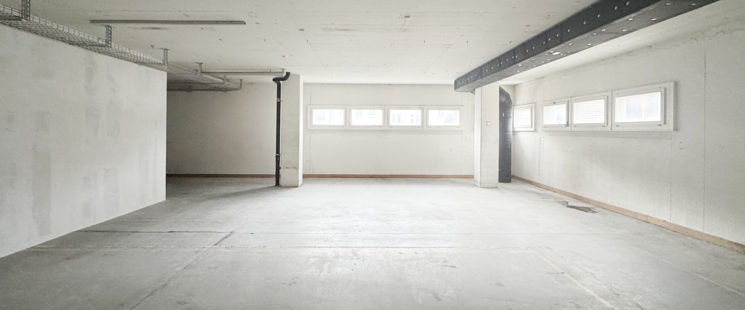 Empty room with a concrete floor, white walls, a pipe on the wall, and multiple windows
