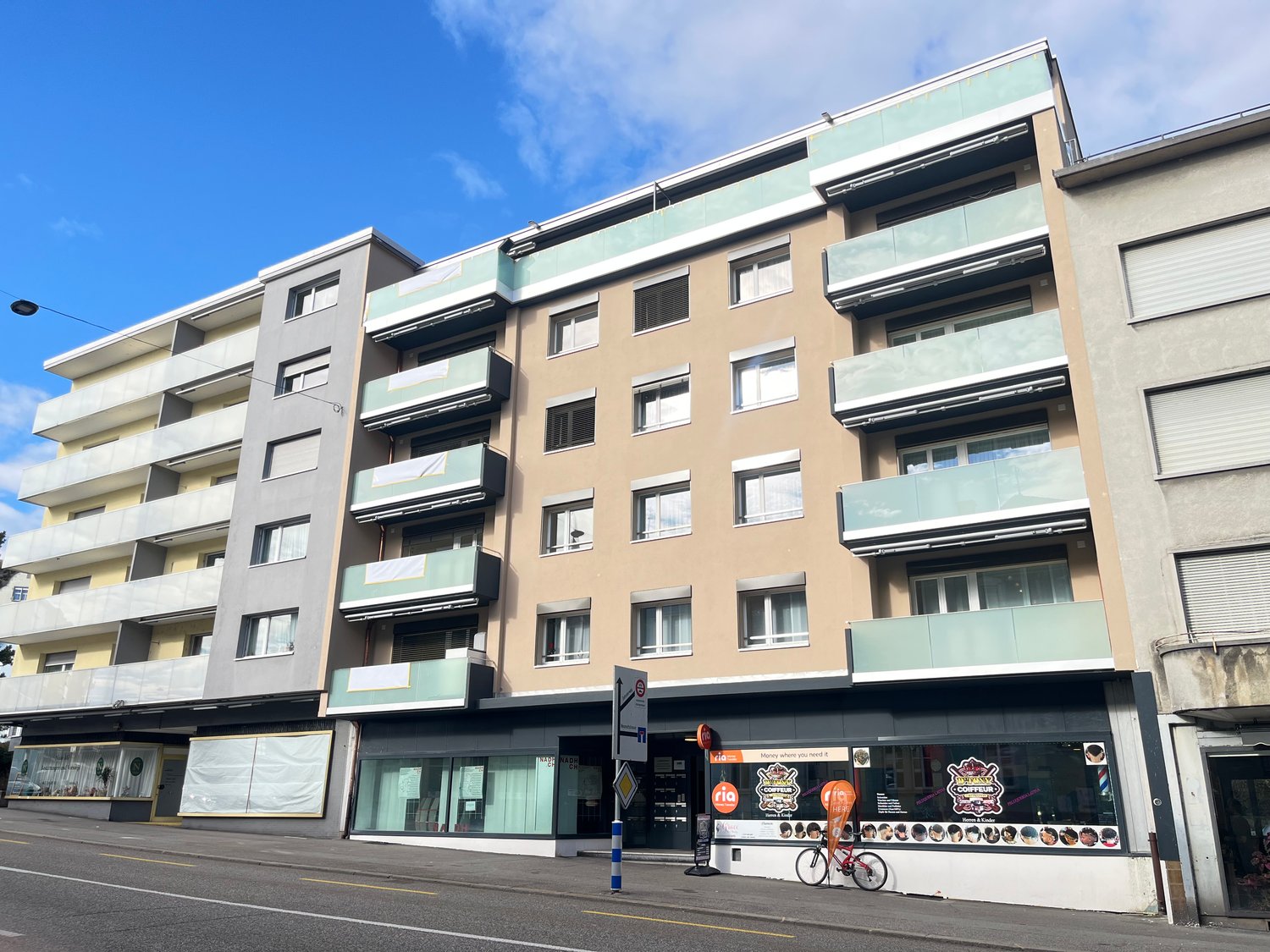 Multi-story residential building, multiple balconies, glass windows, ground floor shops