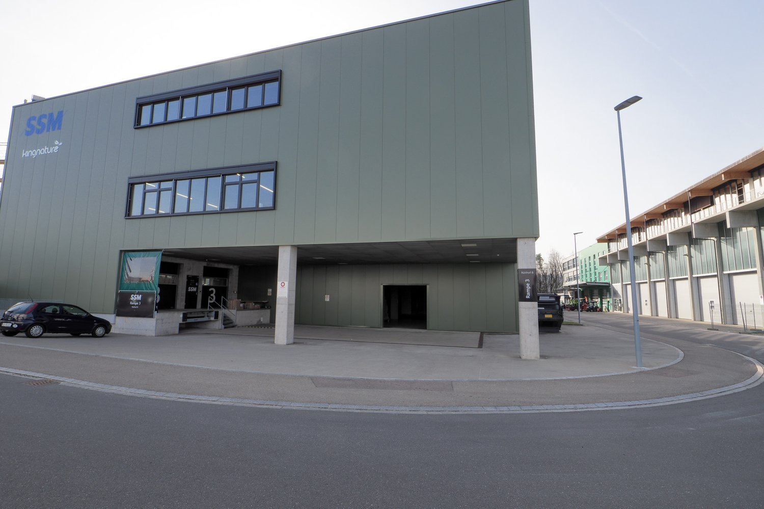 modern commercial building, steel and concrete, green facade, large glass windows, main entrance with glass doors, signage