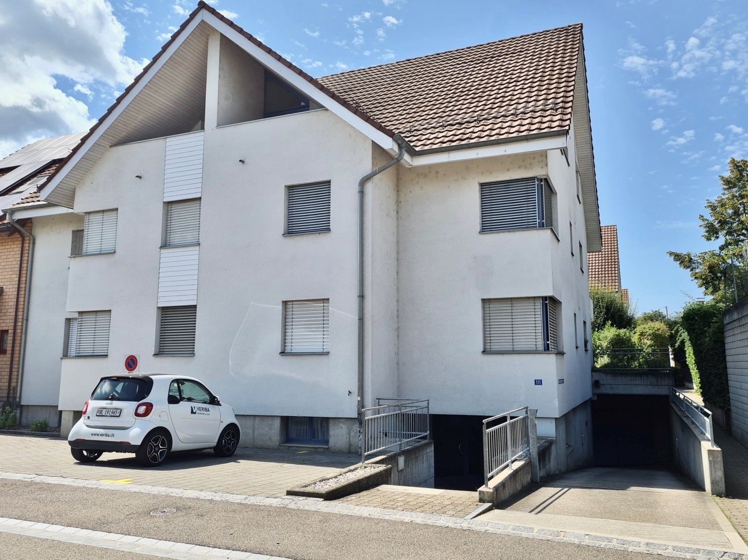 Apartment building with garage, white exterior, red tile roof, solar panels, small car parked in front