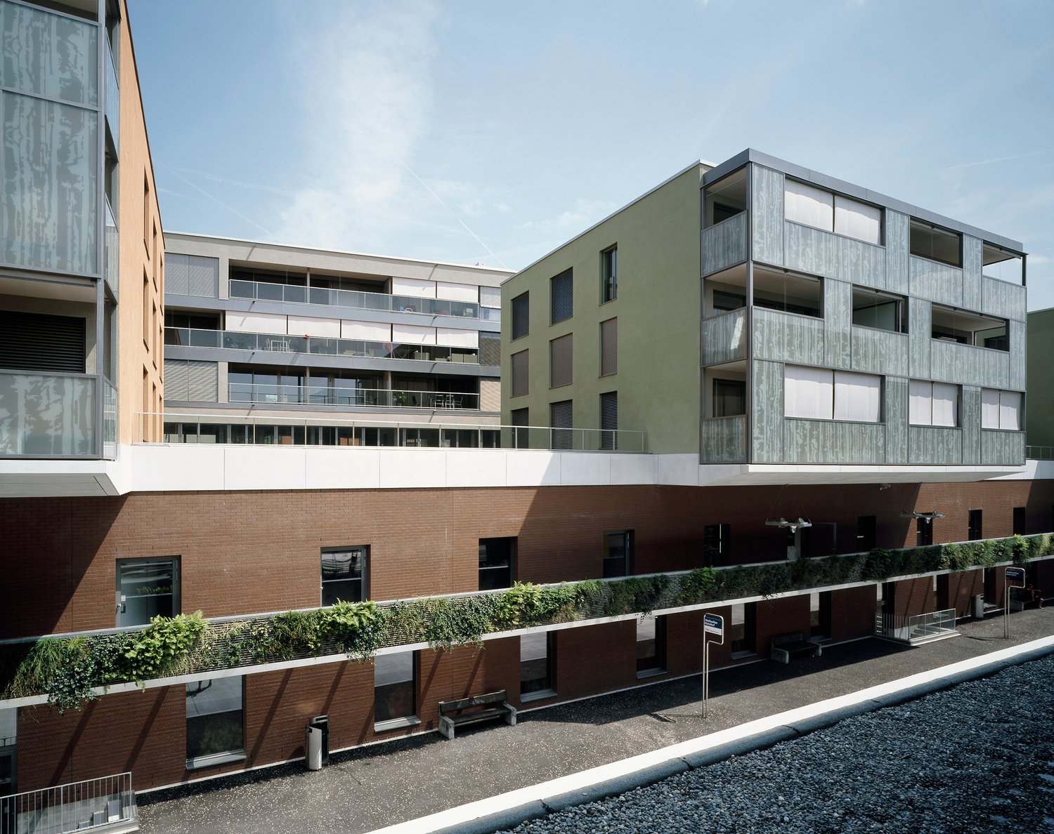 Multi-story apartment building with a modern, minimalist design. The building features a mix of materials including wood, glass, and brick. There are balconies on some of the units, providing outdoor space for the residents. The building appears to be par