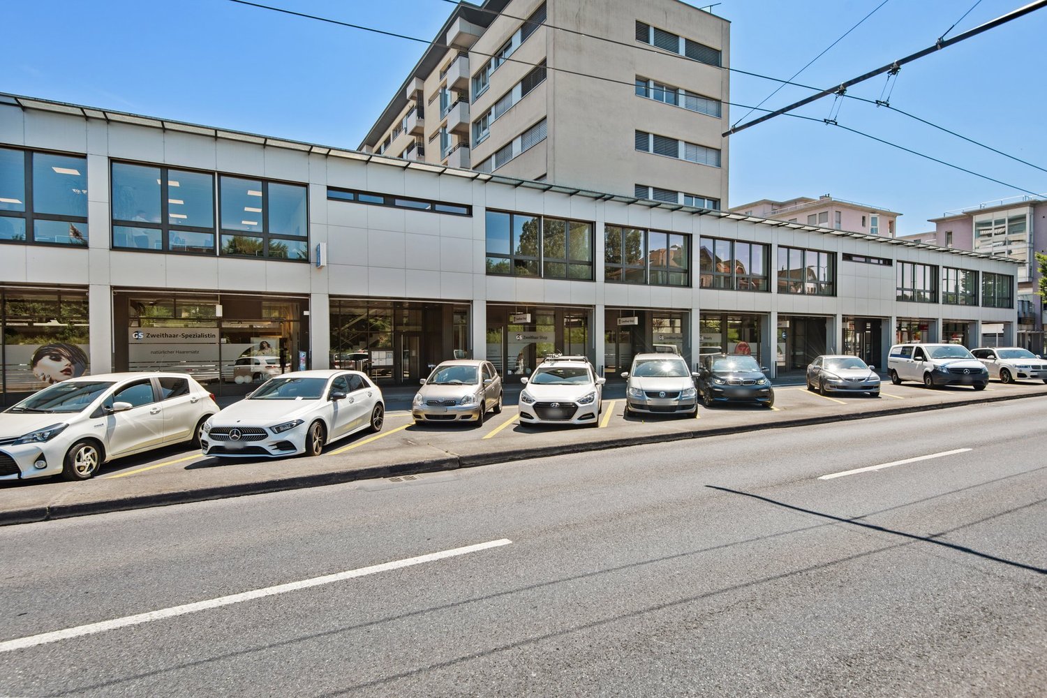 White commercial building with glass facades and several vehicles parked in front