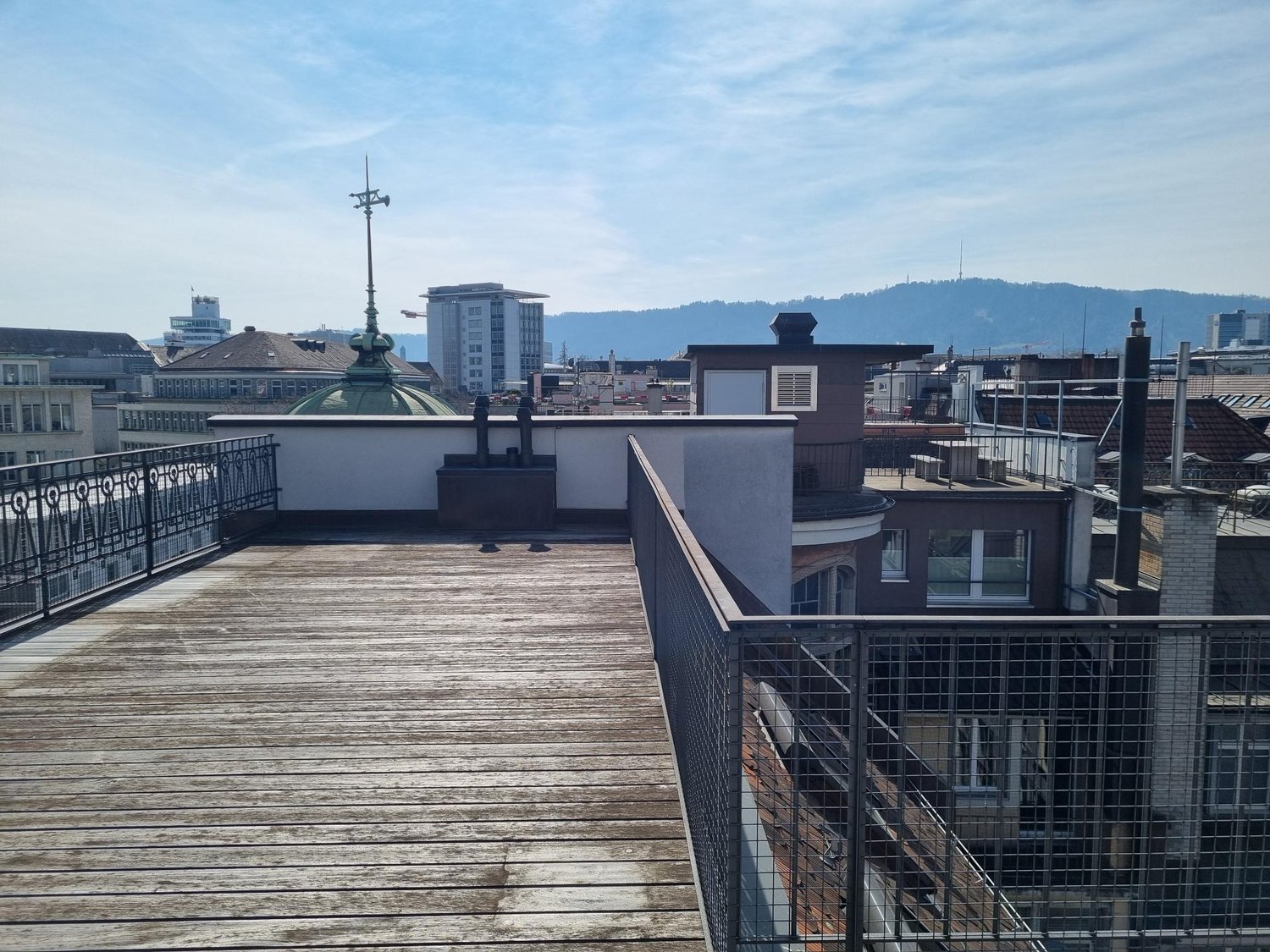 Wooden deck, metal railings, city view, mountains in the distance