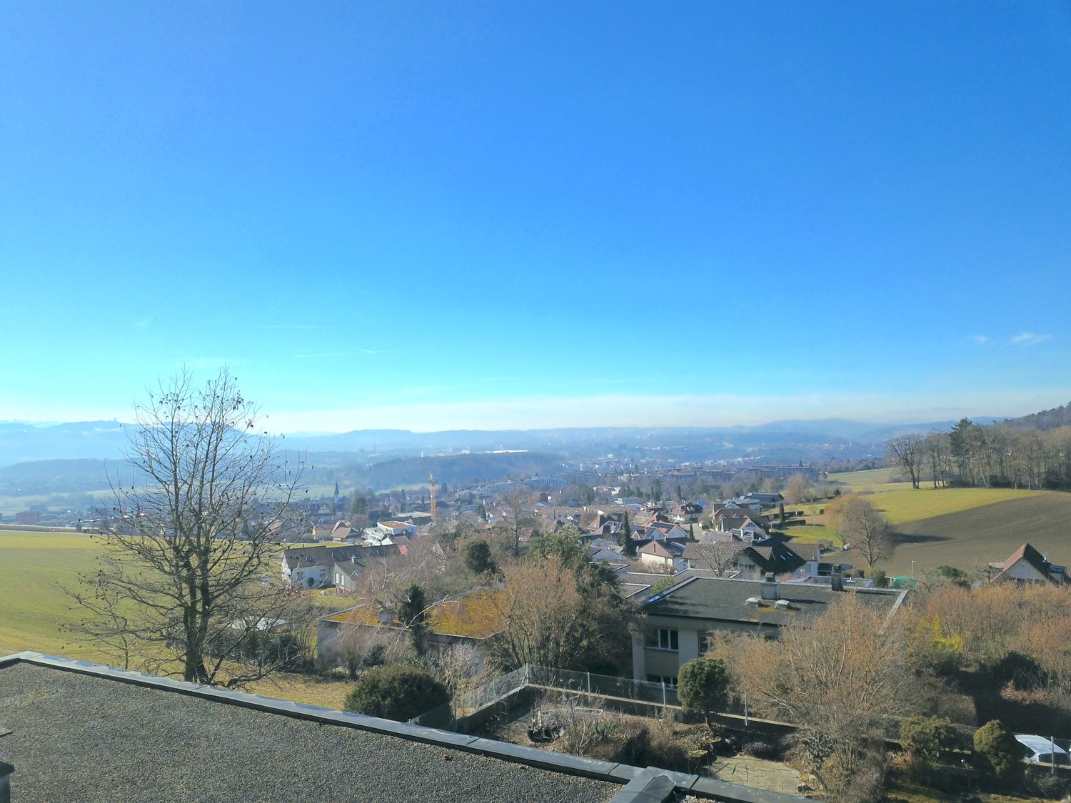 top view of a neighborhood with houses, mountains, and wide valley, rooftops, trees and a road in between