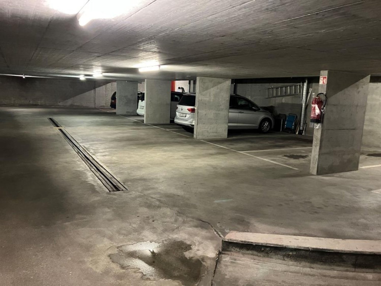 Underground parking garage with concrete walls and floor, several parked cars visible