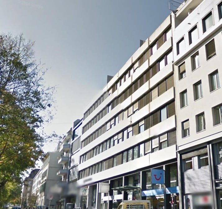 Multi-story building, white exterior, multiple windows, commercial space on the ground floor, trees in the vicinity