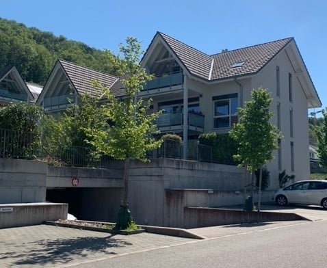 3 story house, gray roof, white walls, garage, balcony, trees, plants, mountain