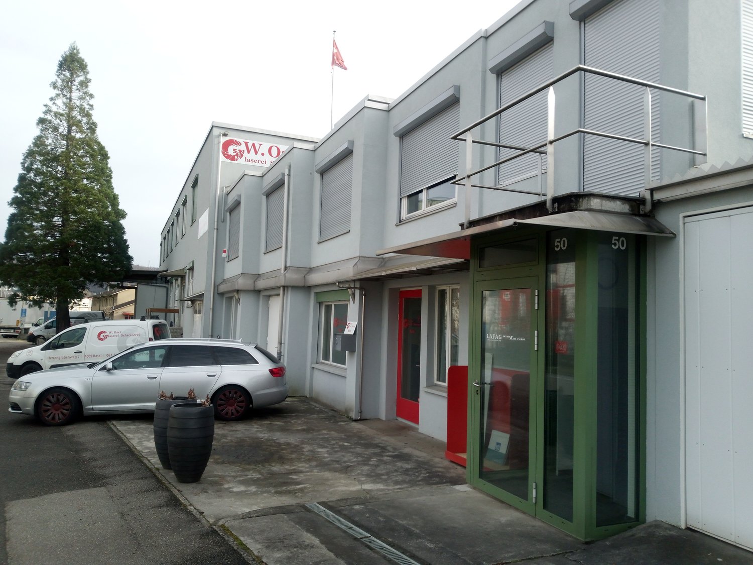 Commercial building with multiple windows, red door, green door, balcony, cars parked in front