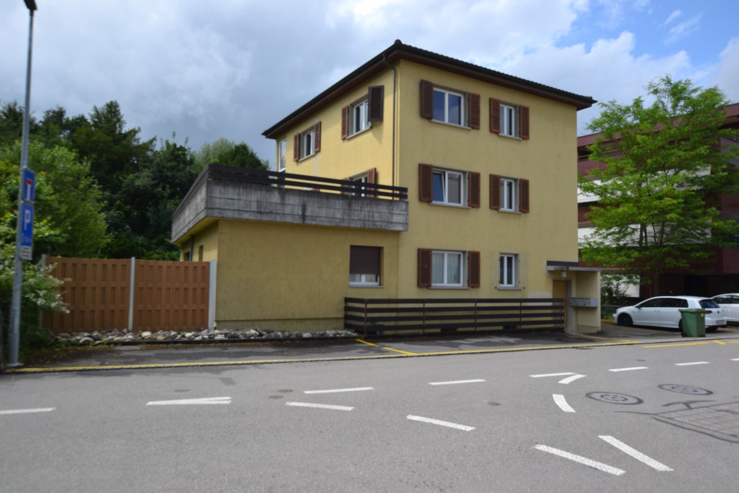 2-story yellow building, balcony on second floor, brown fence, parking spot for 2 cars