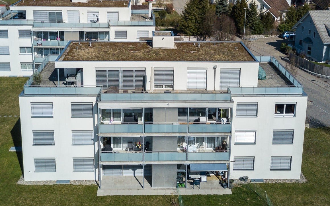 white apartment building, green rooftop, balconies, windows with shutters