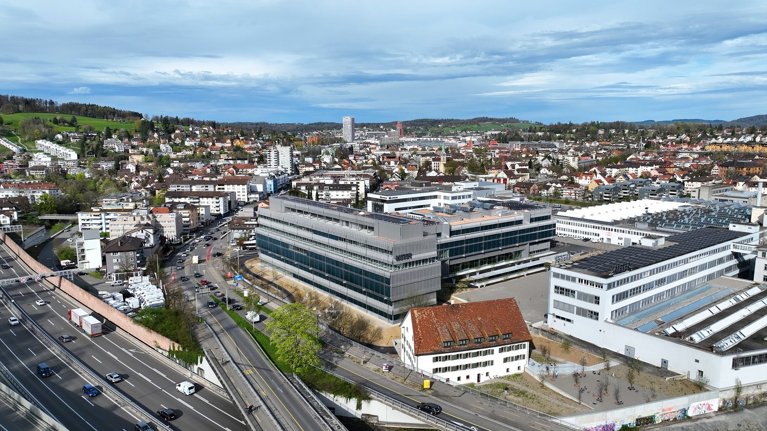 The image shows a panoramic view of a city skyline. The city appears to be a densely populated urban area with a mix of high-rise buildings, residential structures, and commercial buildings. The cityscape is surrounded by hills and mountains in the backgr