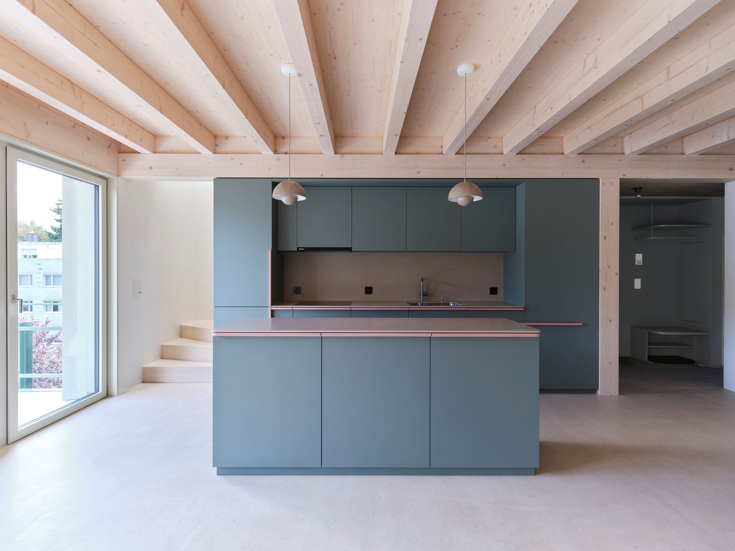 Exposed wooden beams, gray kitchen cabinets, pink countertop, stainless steel sink, modern appliances, sliding glass door, stairs, clean and minimalist design