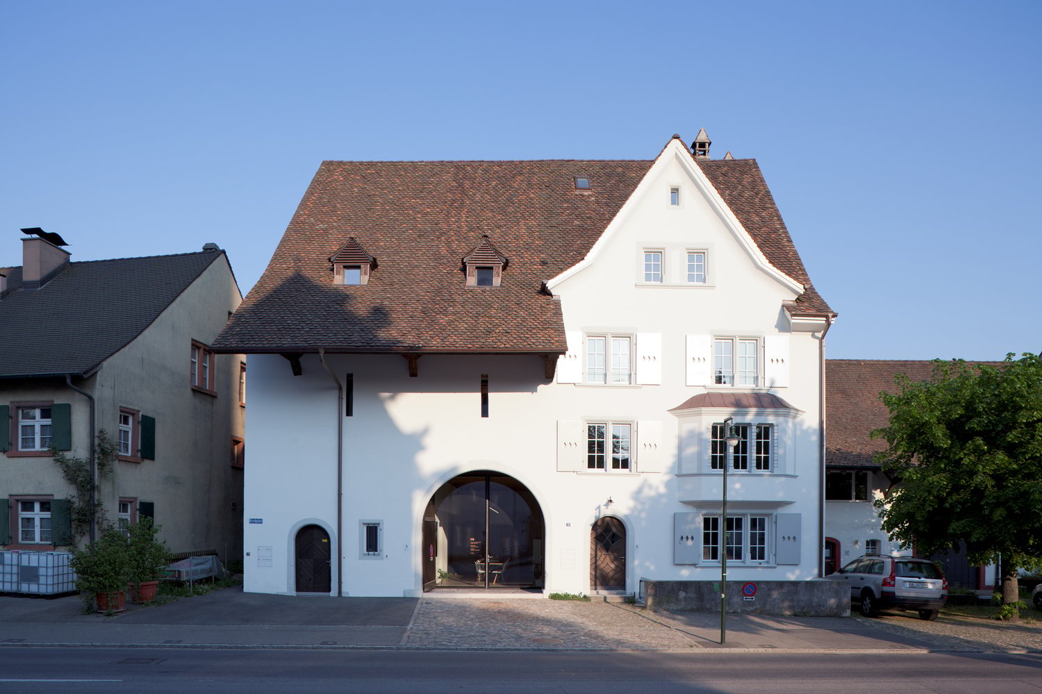 white facade, brown roof, arched entrance, multiple windows, modern design, parking area