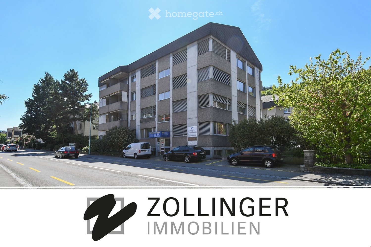3-story building, grey concrete, multiple windows, parking spaces in front