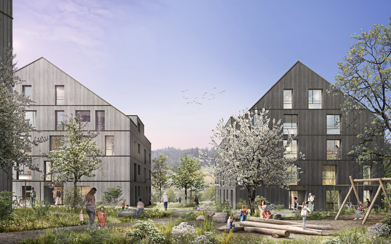 The image shows a residential complex with several multi-story wooden buildings surrounded by a lush, landscaped outdoor area. The buildings have balconies and large windows, and the outdoor space features trees, flowers, and a play area with logs for chi