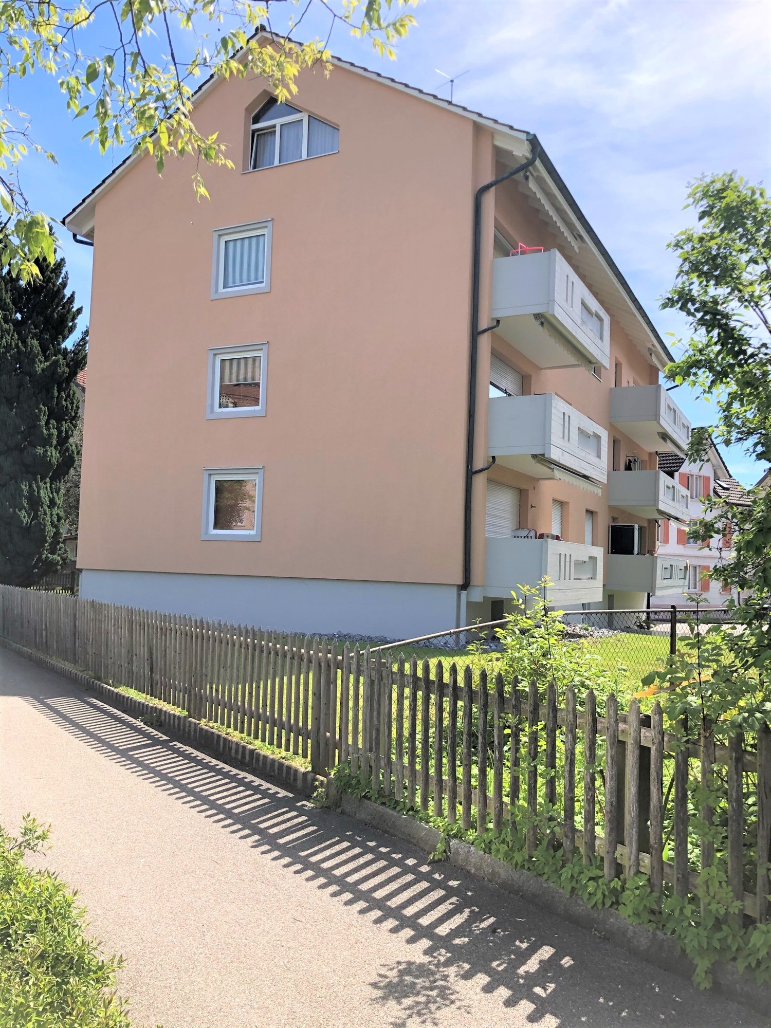 3 story apartment building, pink paint, 3 balconies, wooden fence