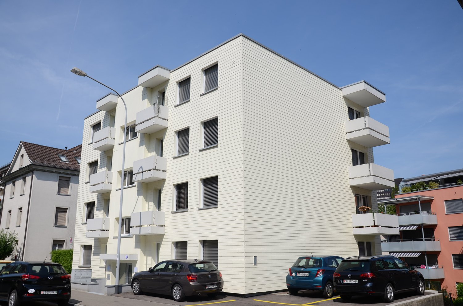 4 story white building, balconies on every floor, car parking in front of the building