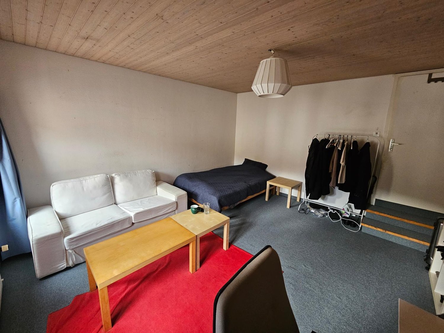 living room with couch, coffee table, bed, storage rack, lamps, blue curtain