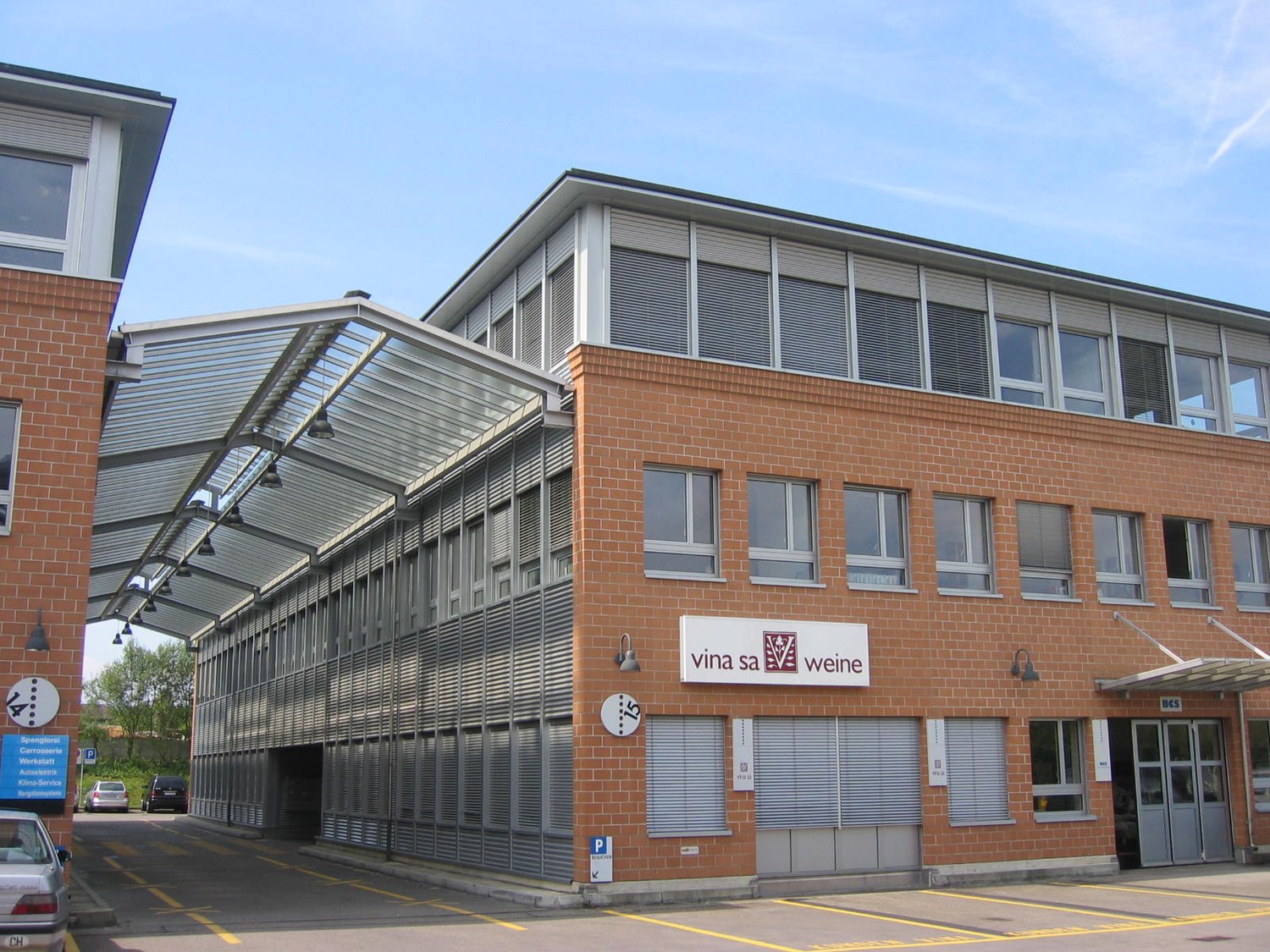 The image shows a multi-story commercial building with a brick facade and large windows. The building has a prominent sign that says 'Vina sa weine', indicating it is likely a wine-related business or facility. The building also has a covered walkway or e
