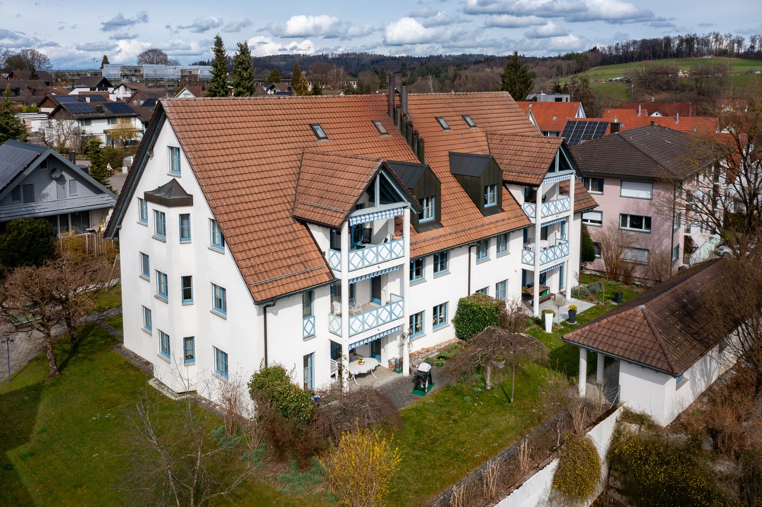 3-story house, brown roof, white walls, blue trim, multiple balconies, multiple windows, garden, solar panels