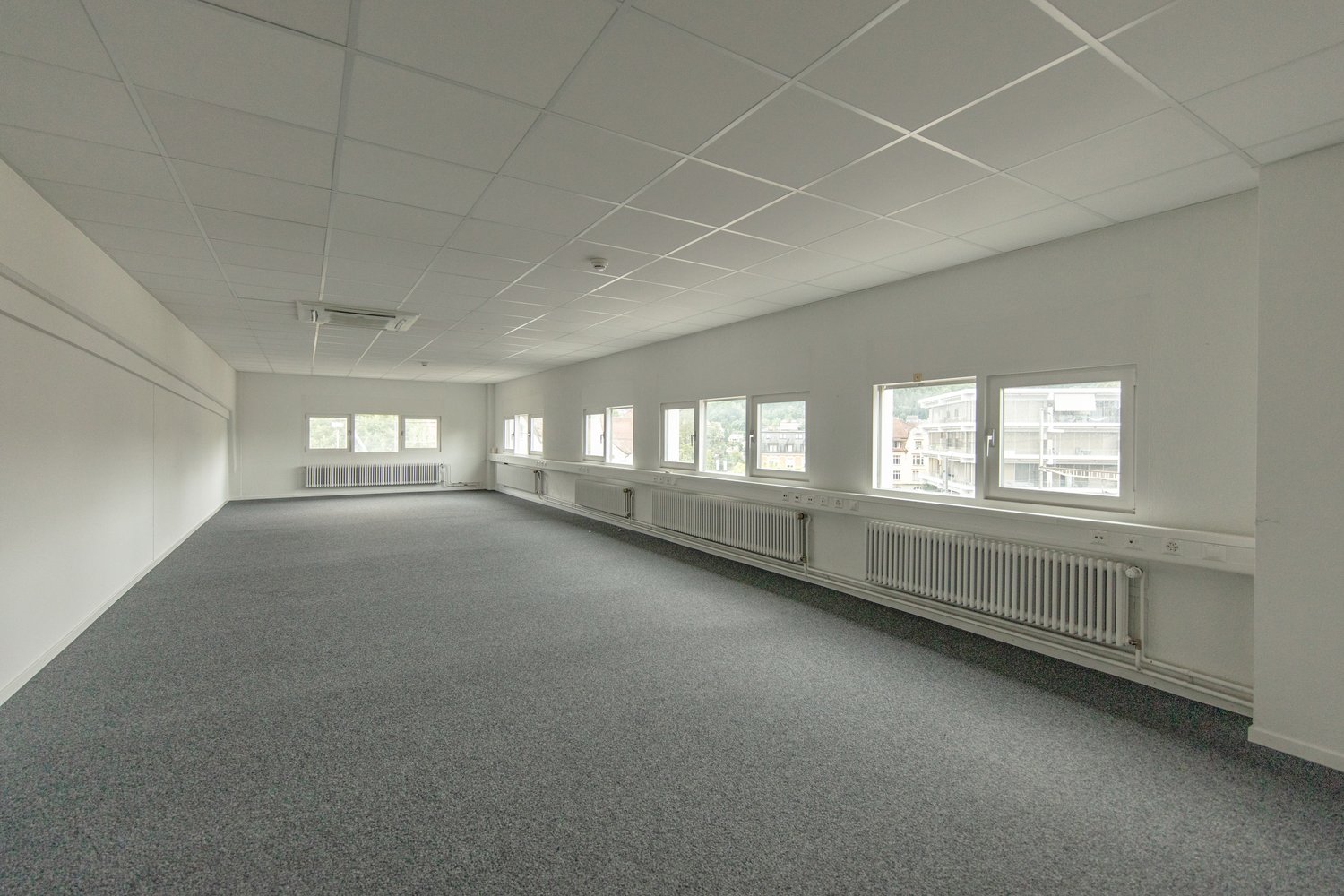 empty office room, white walls, grey carpeted floor, windows, radiators, ceiling with white tiles