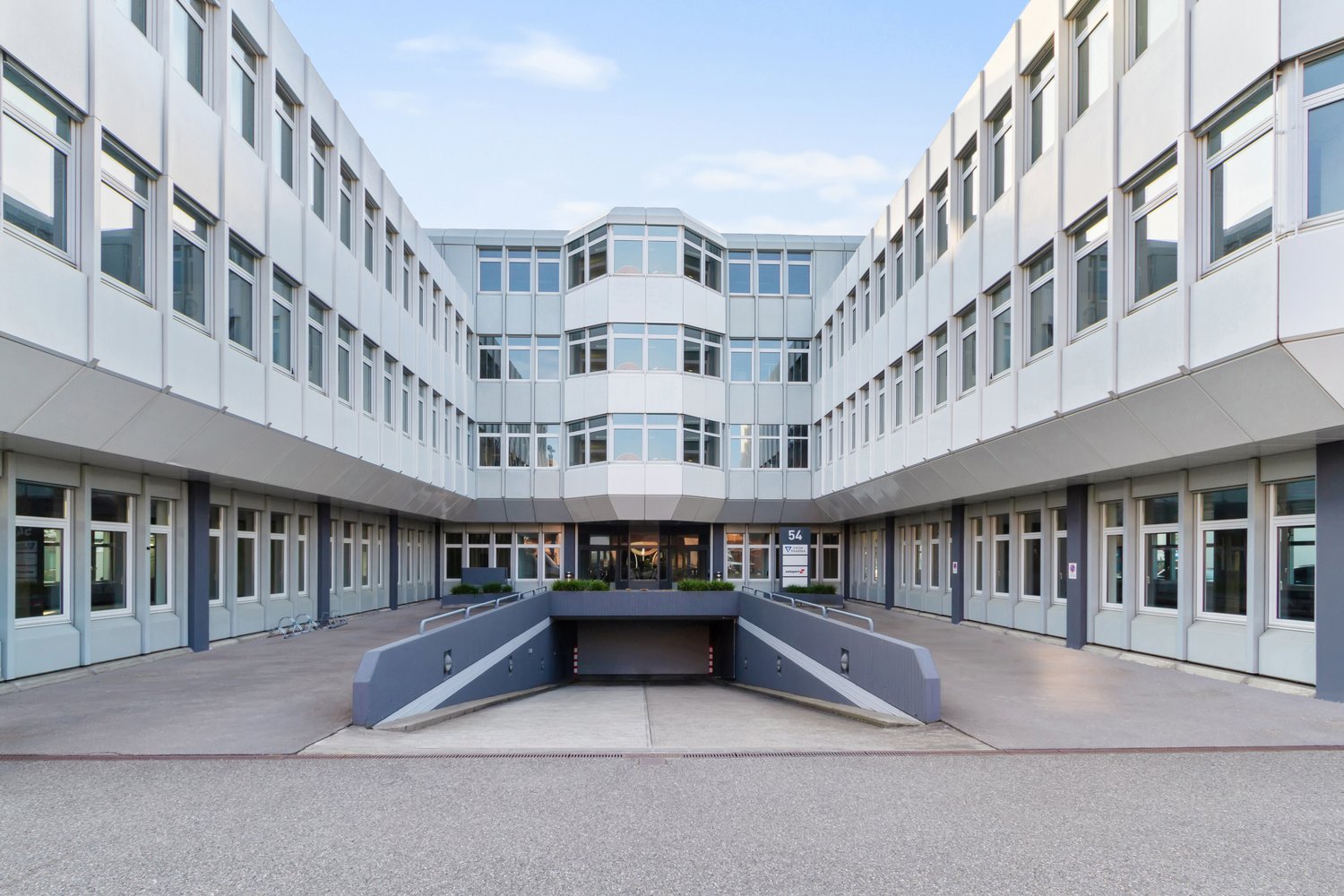 Modern office building, white exterior, multiple floors, large windows, underground parking