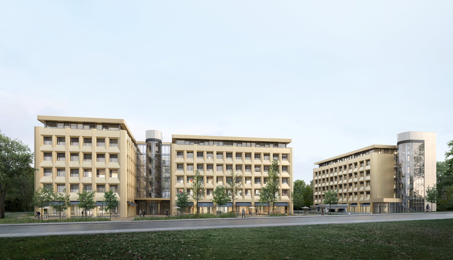 Modern multi-story hotel buildings with many windows, landscaped grounds with grass and trees, paved road in front, staircase entrance, glass wall, awnings over some windows, distant cyclists.