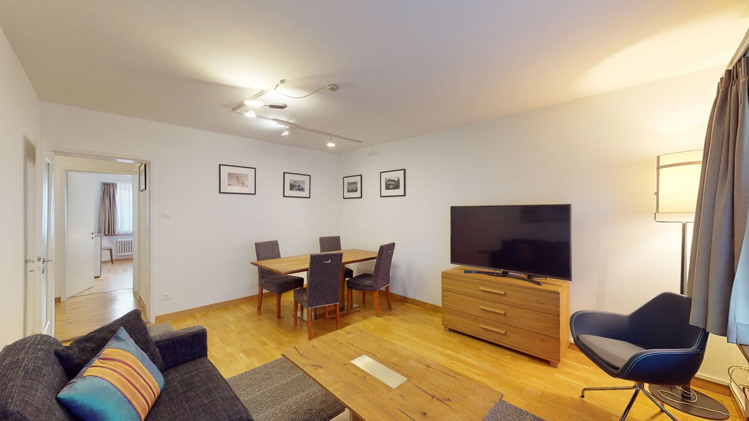 Living room with wooden floor, large windows, dining table, couch, TV, lamp, and modern interior