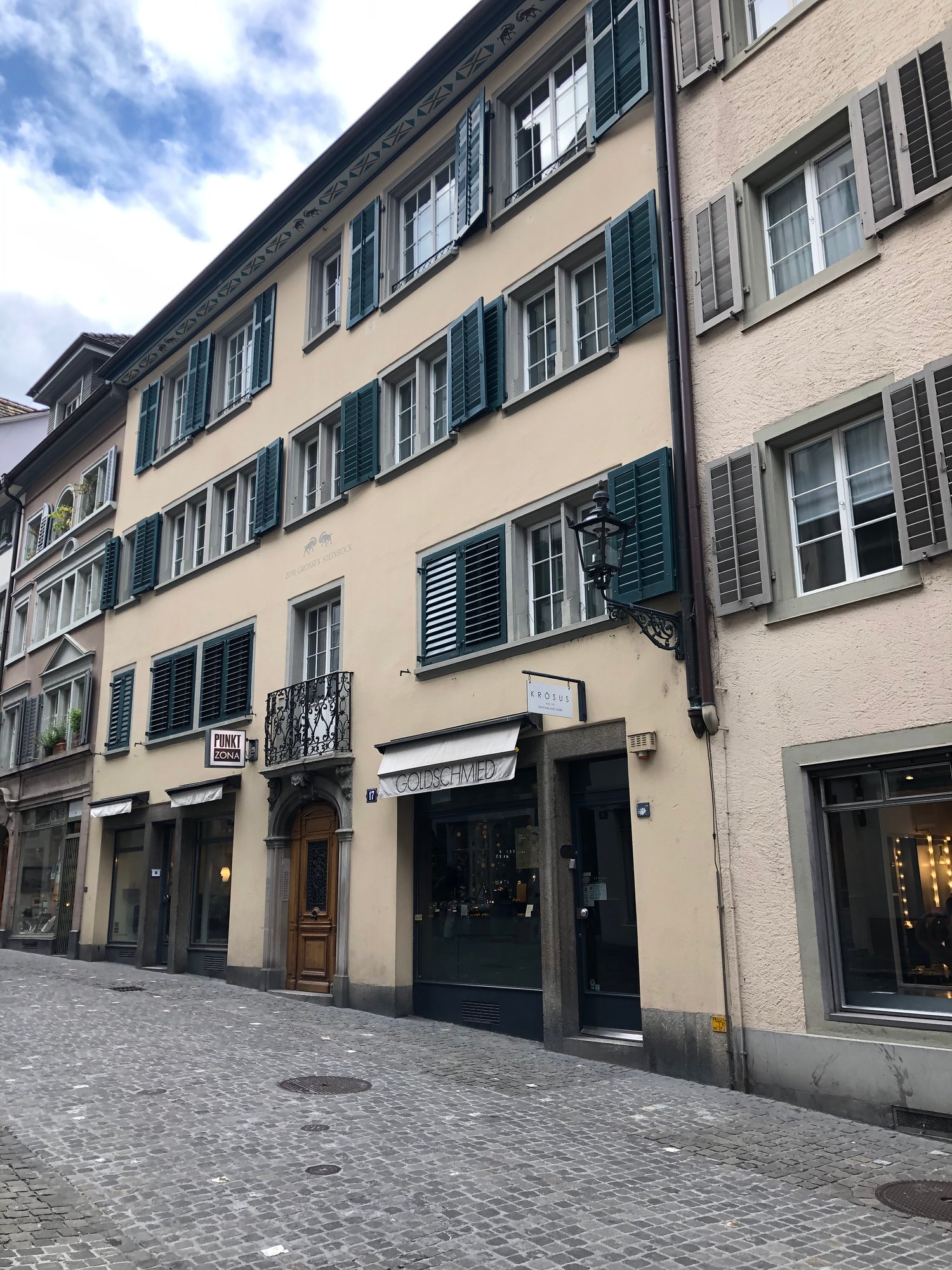 4 story beige building, green shutters, street lamp, entrance to shops