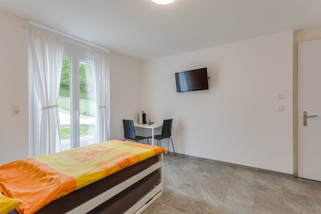 bedroom with bed, desk, chairs, television, curtains, tiled floor