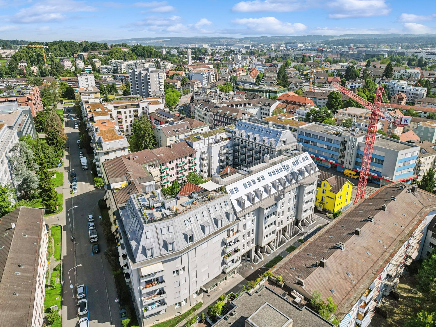 Aerial view of multiple residential buildings, some with rooftop terraces, gray roofs, street with cars, city view