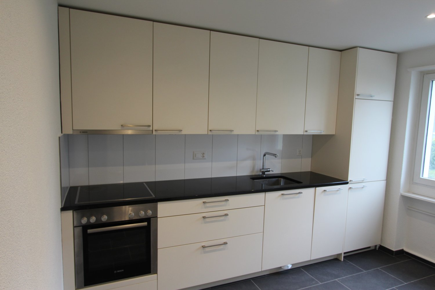 modern kitchen with white cabinets, black countertops, stainless steel oven, sink with faucet, electrical outlets