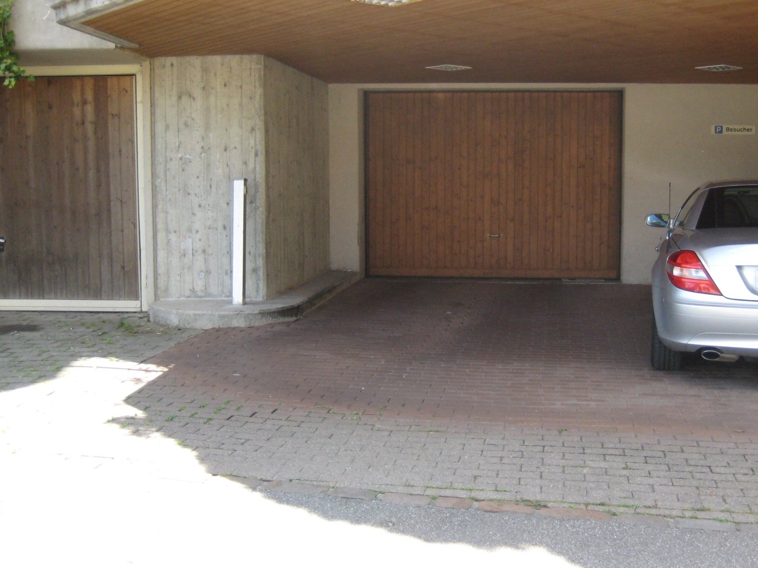 Garage space with a wooden door, brick floor, and parked car.