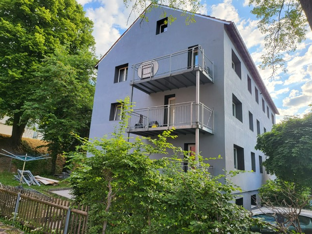 3 story house, gray exterior, metal balconies, surrounded by trees