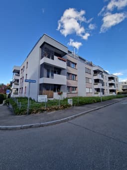 4-story modern apartment building with gray exterior, balconies, and landscaped grounds