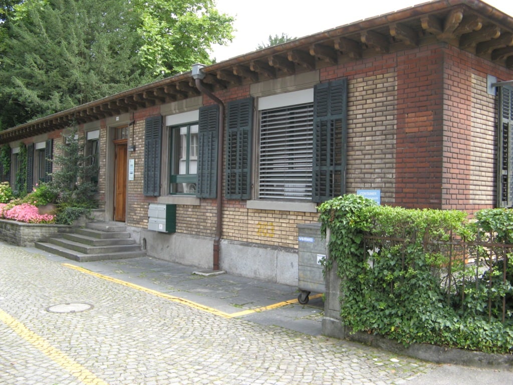 Brick building, black shutters, small garden, brown wooden door, paved walkway