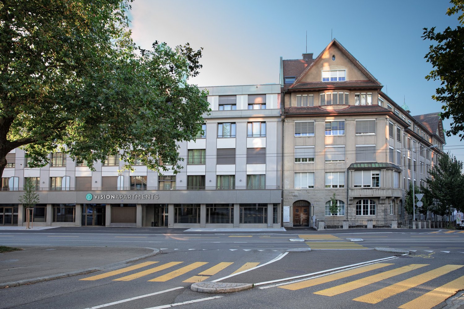 Modern building with many windows, entrance with glass doors, large sign reading 'VISIONAPARTMENTS'.