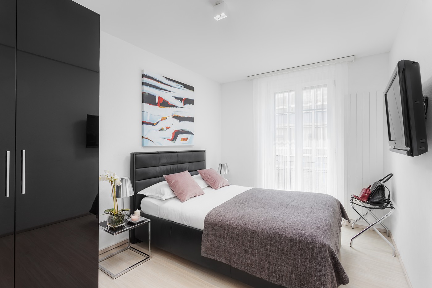 Modern design with white walls, black furniture, double bed, bedside tables with lamps, TV, painting, nightstand with candle and flower vase