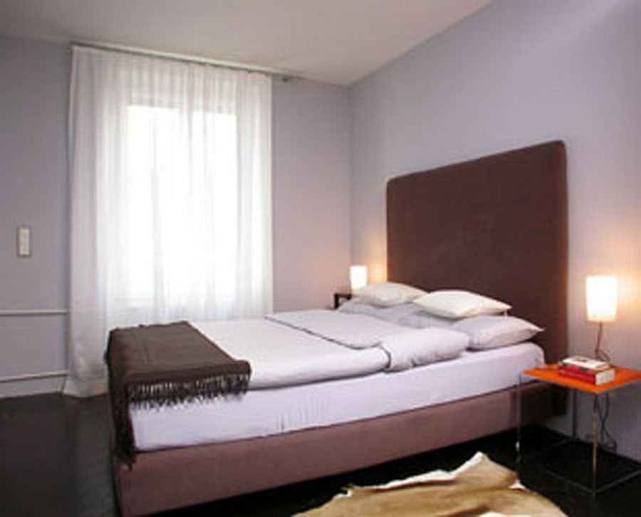 double bed, brown headboard, white curtains, white walls, bedspread, pillows, blanket, nightstands, lamps, rug