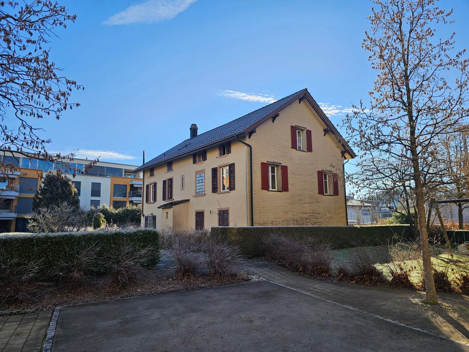 2 story house, yellow brick, red shutters, driveway, hedges, trees