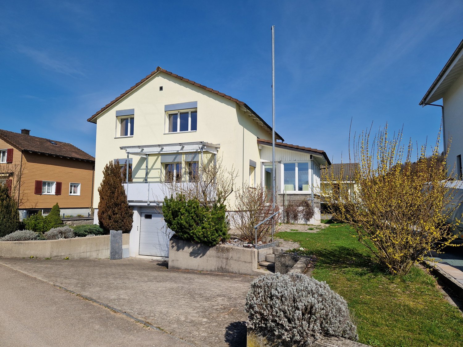 2 story house, yellow exterior, brown roof, garage, balcony, driveway, garden